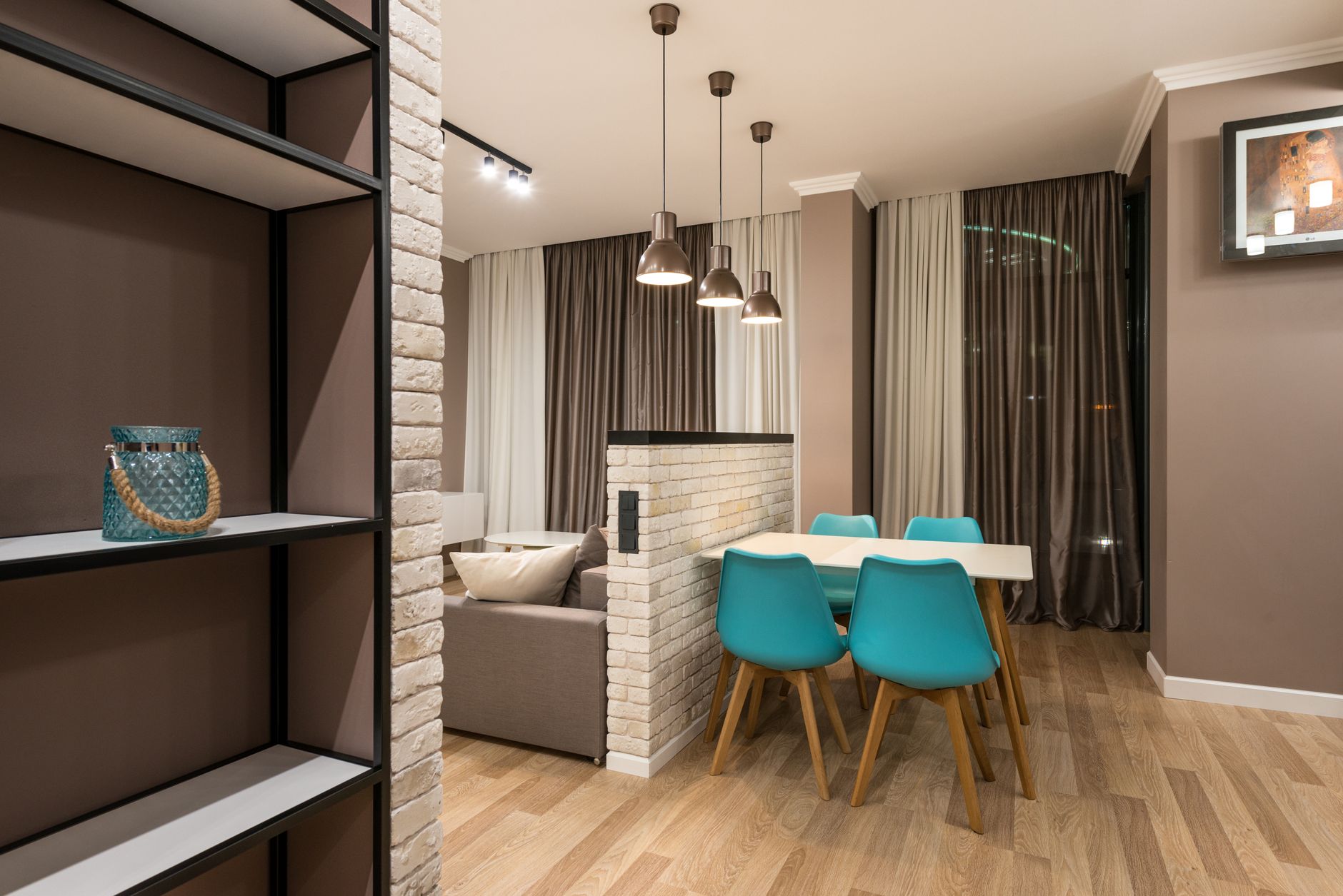 Un salón-comedor de planta abierta delimitado visualmente por una alfombra grande y una estantería abierta que separa sutilmente los espacios.